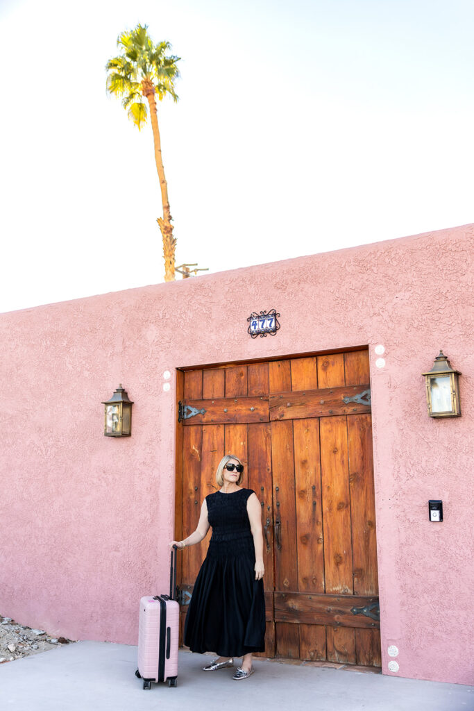 A photo for a Palm Springs guide shows a woman in a black dress outside a pink stucco building 