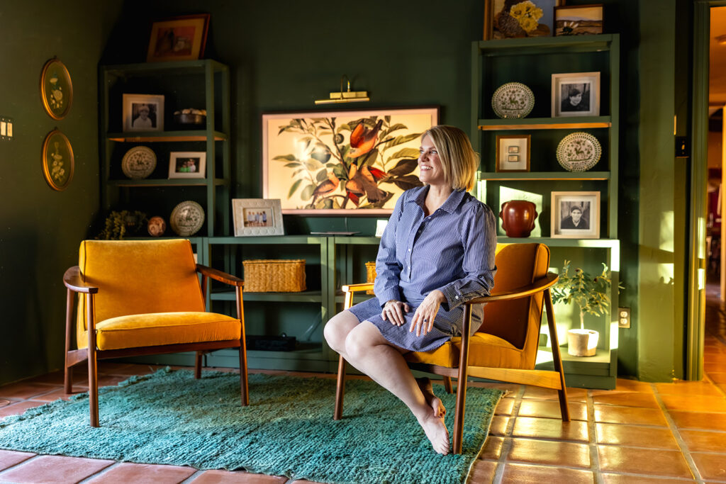 A woman is seated on MCM inspired furniture in the green living room of a Palm Springs home 