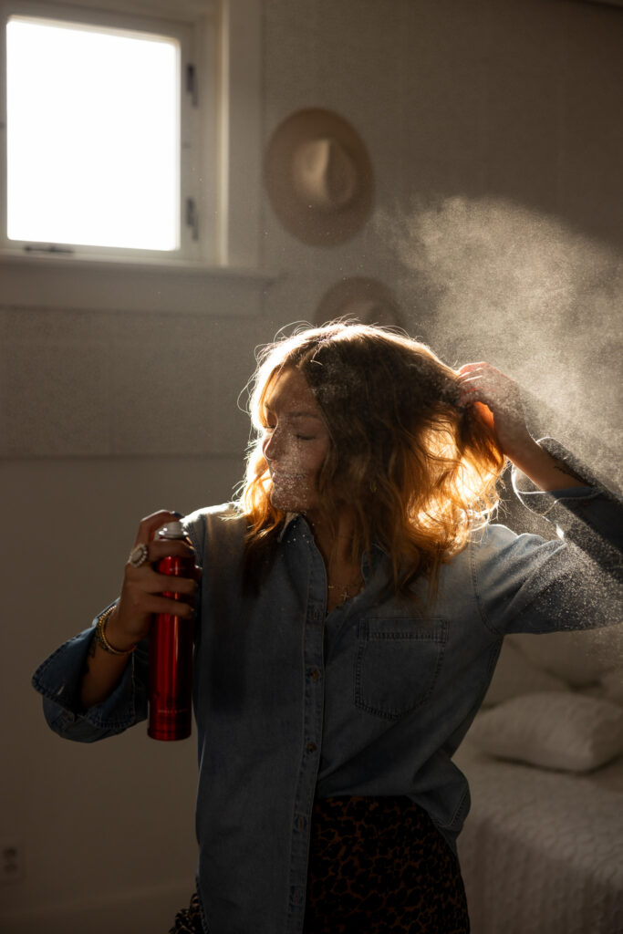 young women spraying hairspray on her hair