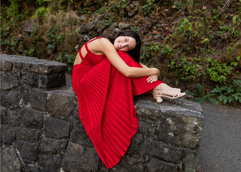 Senior girl in a red pleated dress sitting on a stone wall during a Flodesk review blog about photography marketing
