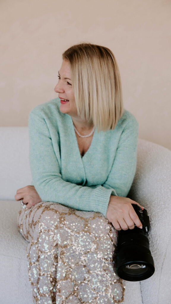 Photographer smiling on couch holding camera, showcasing organized workflow with Dubsado for photographers in action