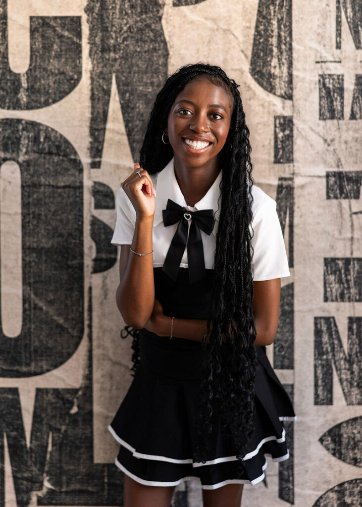 Smiling woman with braided hair posing confidently against textured wall background, natural and relaxed portrait