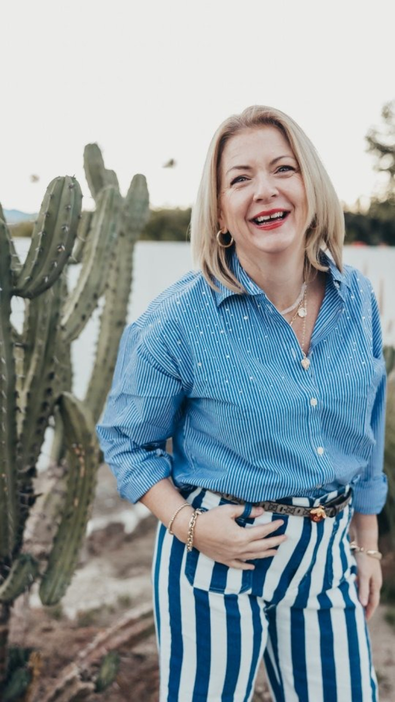 A business owner smiles beside a tall cactus during a lifestyle brand photography session. Her bold striped outfit and relaxed expression create an approachable, professional image that demonstrates effective marketing ideas for photographers promoting personal branding services.