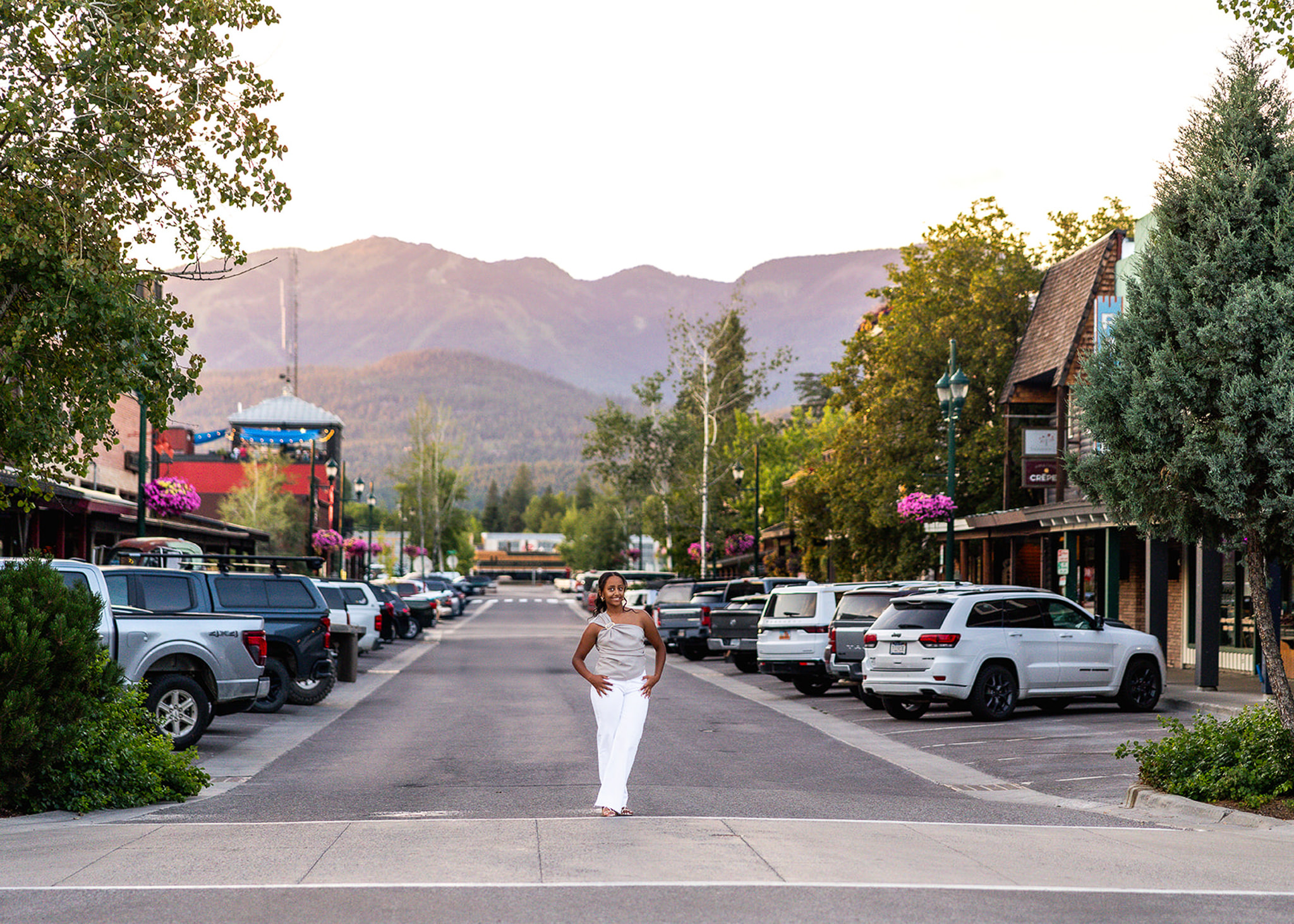 A senior poses confidently in the center of a mountain town street with scenic peaks rising in the background. The combination of architecture, leading lines, and landscape creates a destination senior portrait filled with adventure and personality.