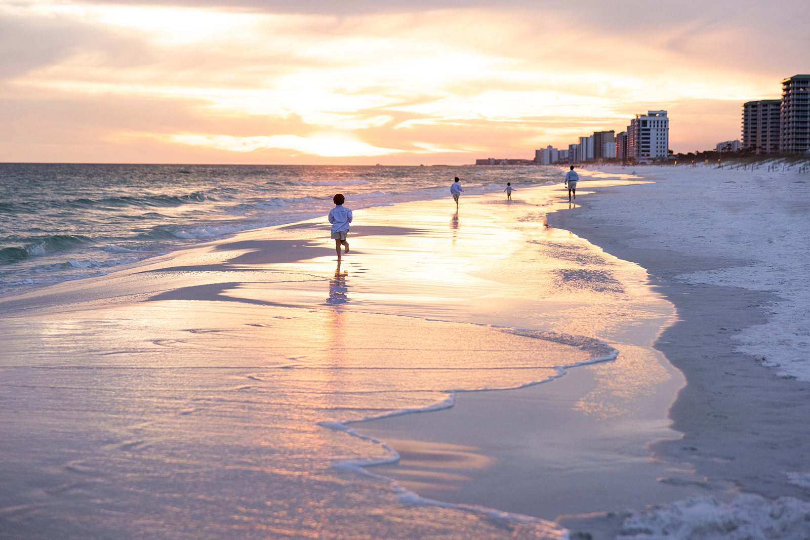 Children run along the shoreline at sunset during a destination photo shoot, creating candid moments as waves roll onto the beach and golden light reflects across the water for a peaceful coastal scene.