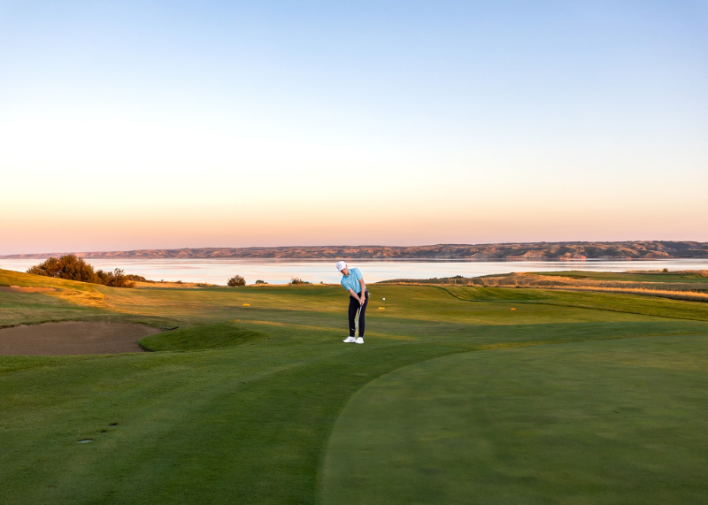 Senior golfer putting on a lakeside golf course at sunset during a personalized senior portrait session.