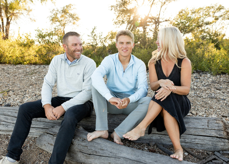 Senior laughing with parents on a driftwood log during a family portrait, highlighting unique senior sessions and connection.